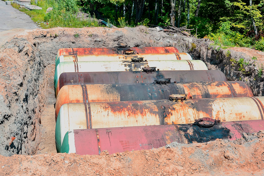 Corroded underground oil tanks exposed in an excavation trench during removal, showing rust and contamination risks.